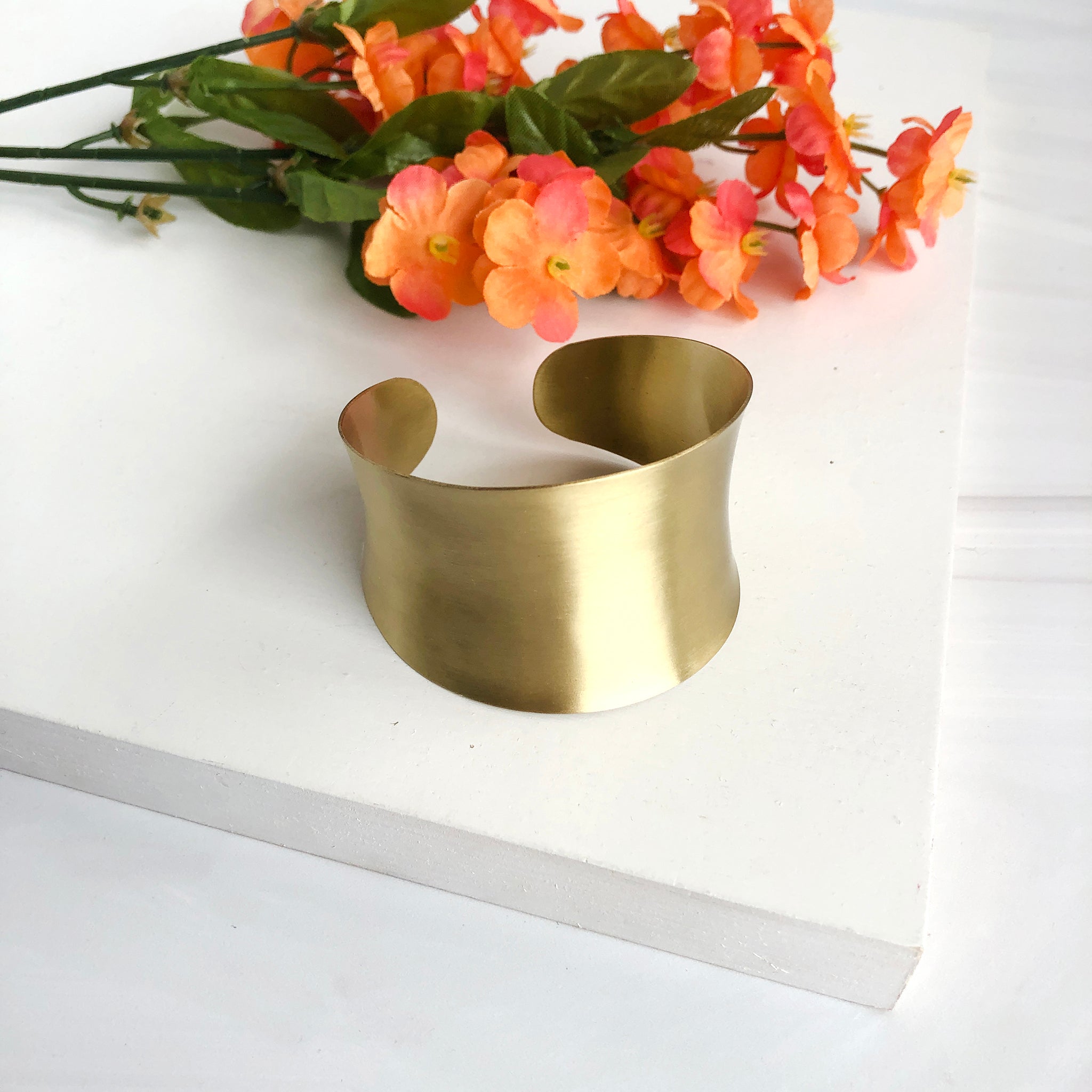 A tall gold cuff bracelet is seen with some orange flowers.