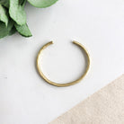 A single gold cuff bracelet is shown, the light highlighting the hammered texture.