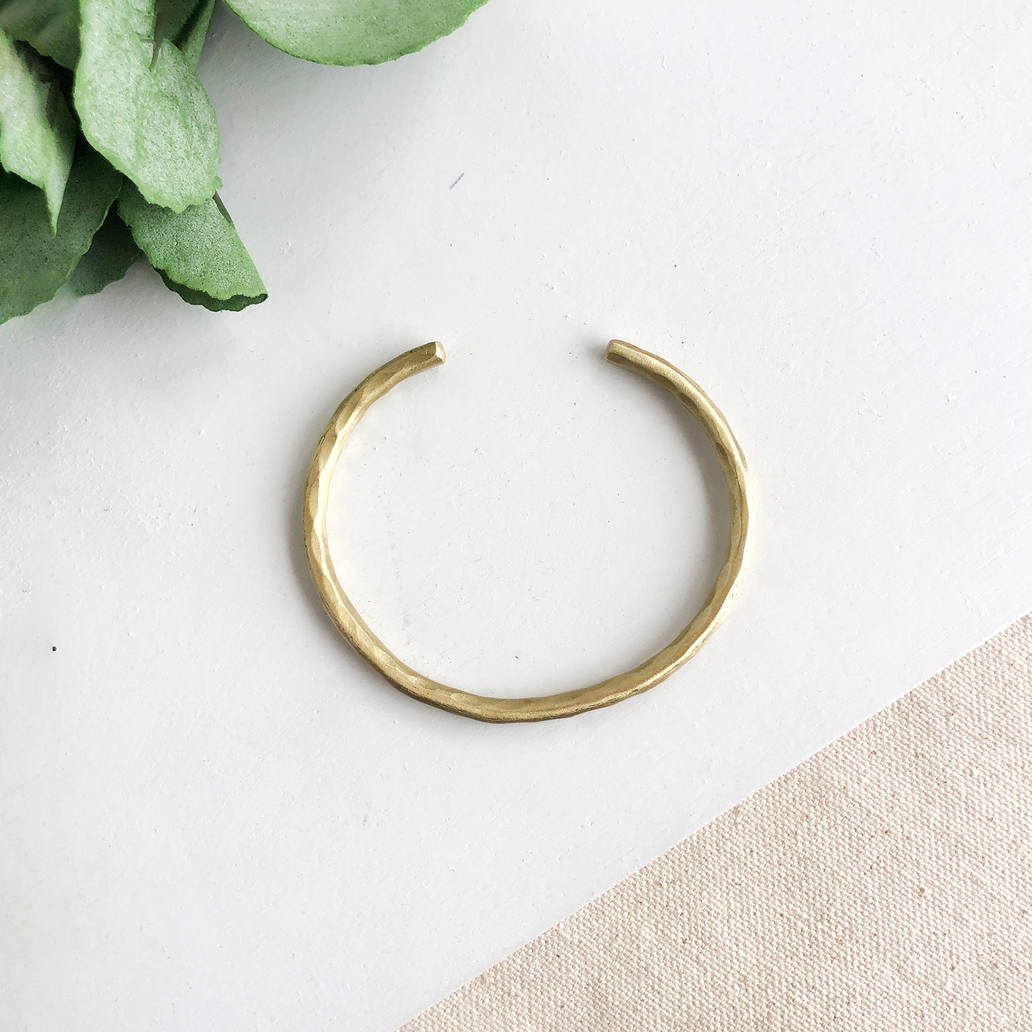 A single gold cuff bracelet is shown, the light highlighting the hammered texture.