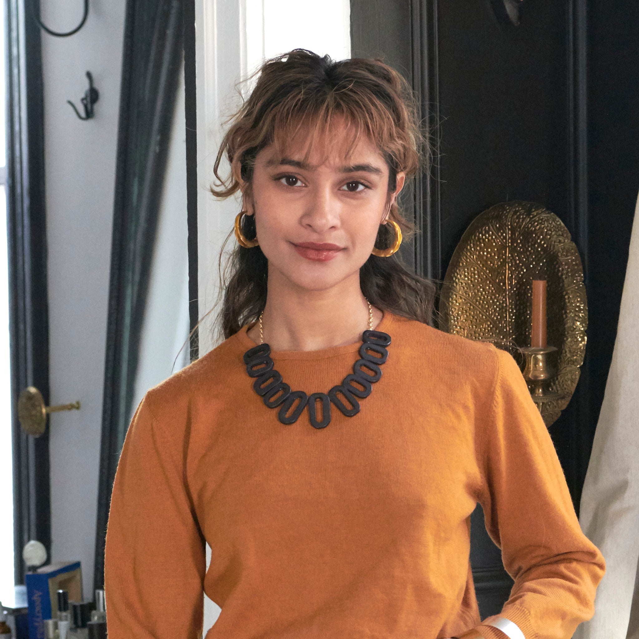 A woman smiles at us while modeling a black necklace and a pair of gold earrings.