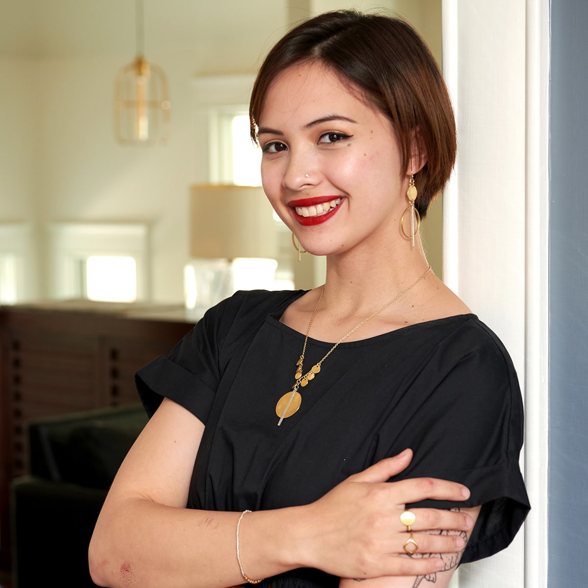 A woman in a black dress is smiling, while modeling a shiny gold pendant necklace and matching earrings.