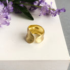 A single gold ring is shown. The sculptural technique gives it a smooth, rounded outer edge with a subtle indent in the center.