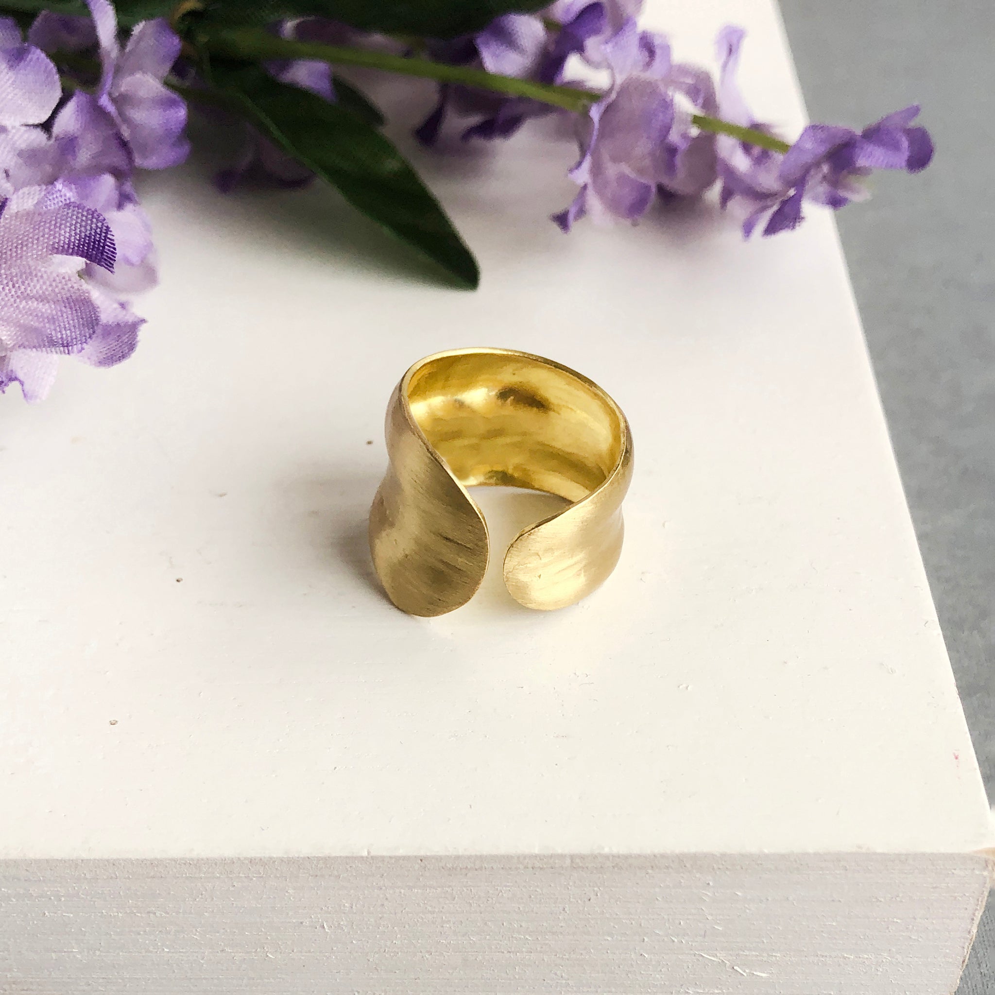 A single gold ring is shown. The sculptural technique gives it a smooth, rounded outer edge with a subtle indent in the center.