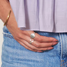 A woman hooks her thumb into her pocket, showing the details of her two silver rings on her fingers.