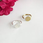 A gold and silver ring, with a large circle center motif, are shown against a white background with a pink flower.