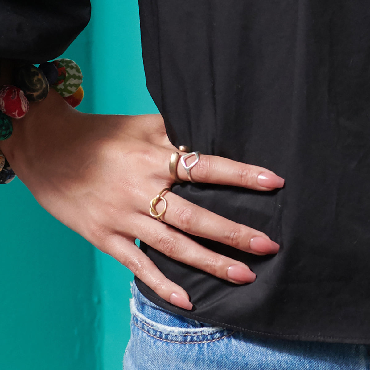 A woman in a black top rests her hand on her hip, showing off her gold and silver rings.