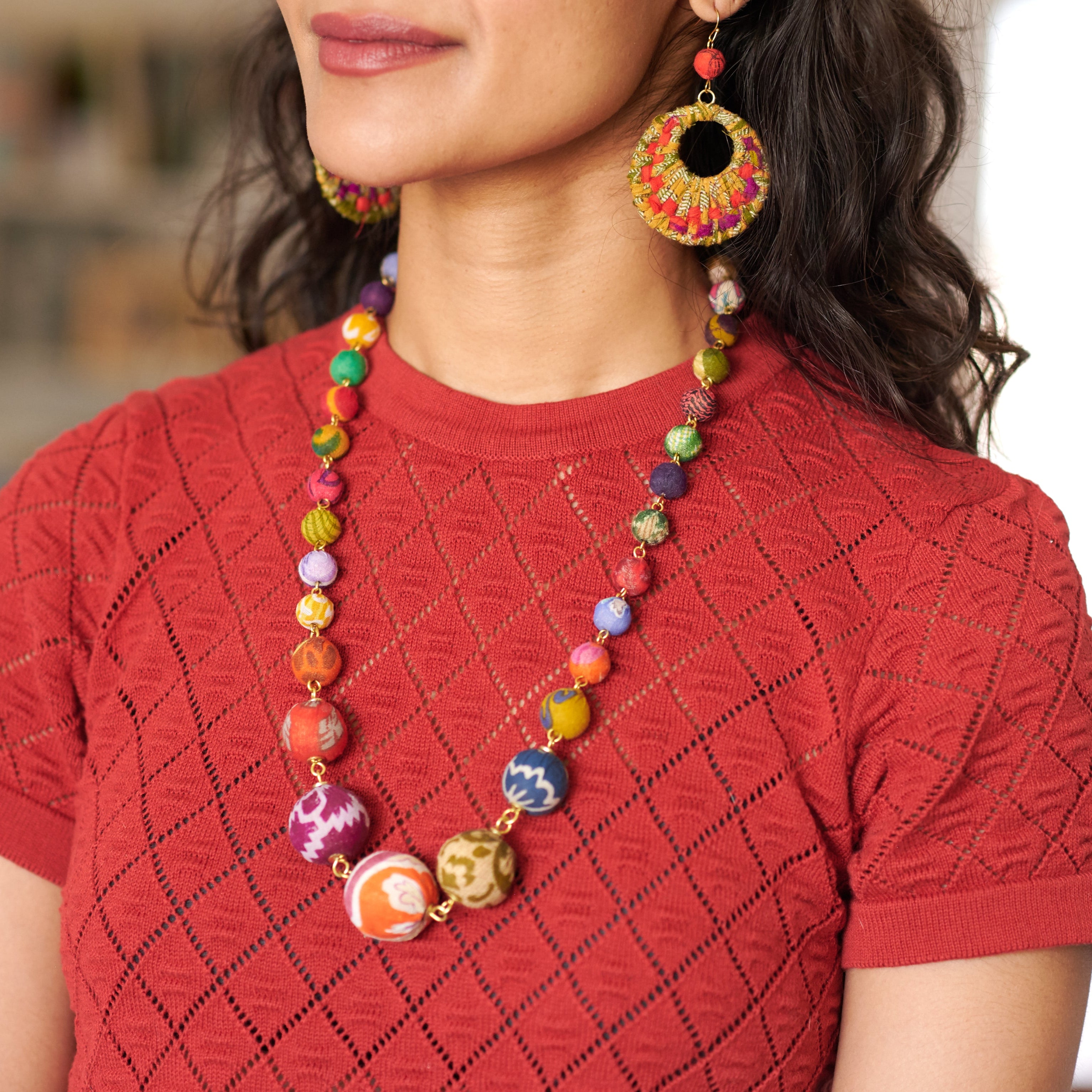 Person wearing a colorful necklace and earrings on a blurred background