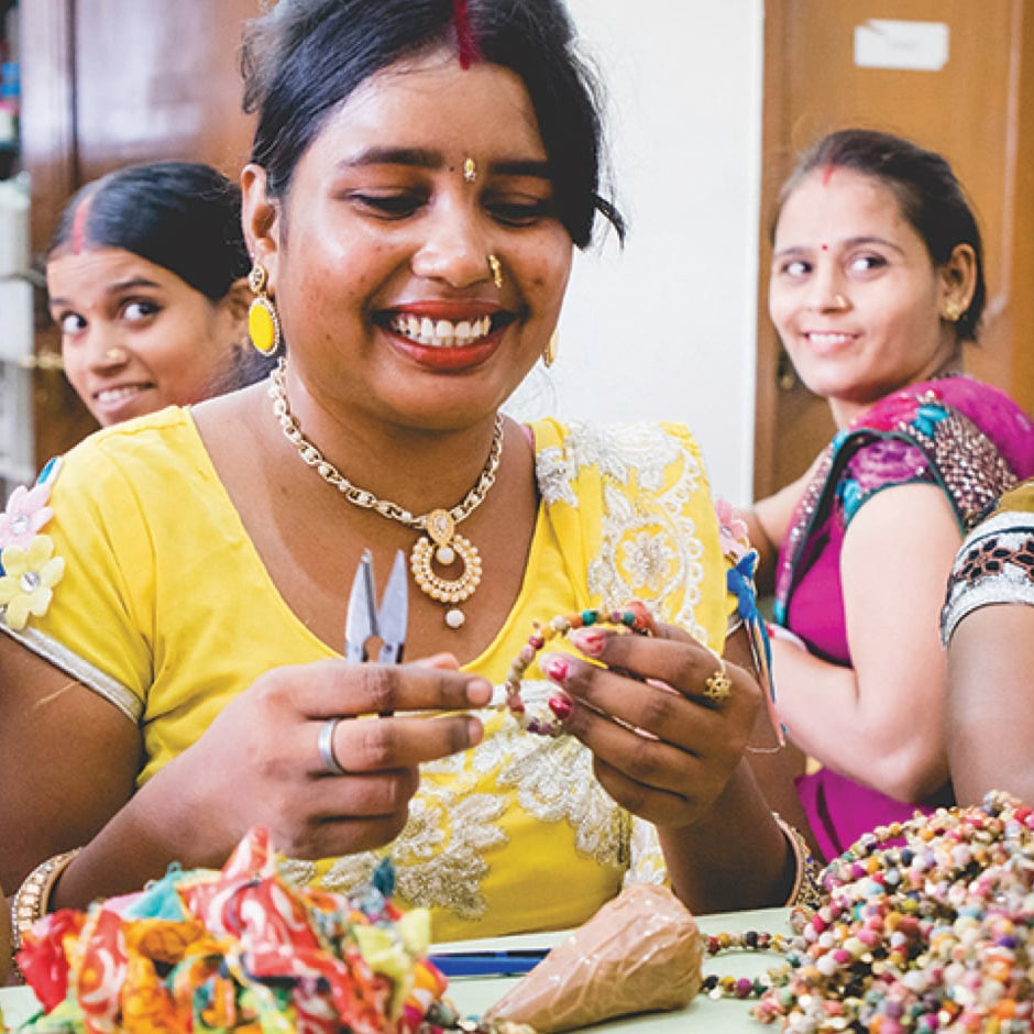 Three women artisans laugh while working amongst completed Kantha bracelets.