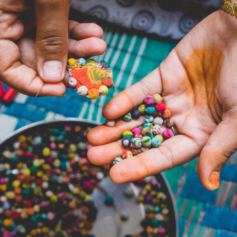 In one hand, an artisan holds an unfinished earring. In the other, a pile of Kantha beads.