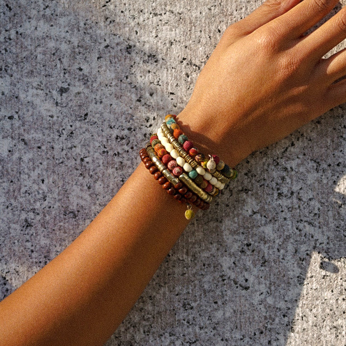 A close up of a woman's arm and her colorful, multi-texture bracelet is shown against a concrete background.