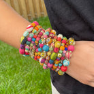 A close up of a woman's wrist, showing the large stack of twelve multicolored bracelets she is wearing.