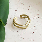 A gold ring rests on a white speckled surface with a green leaf on the left.