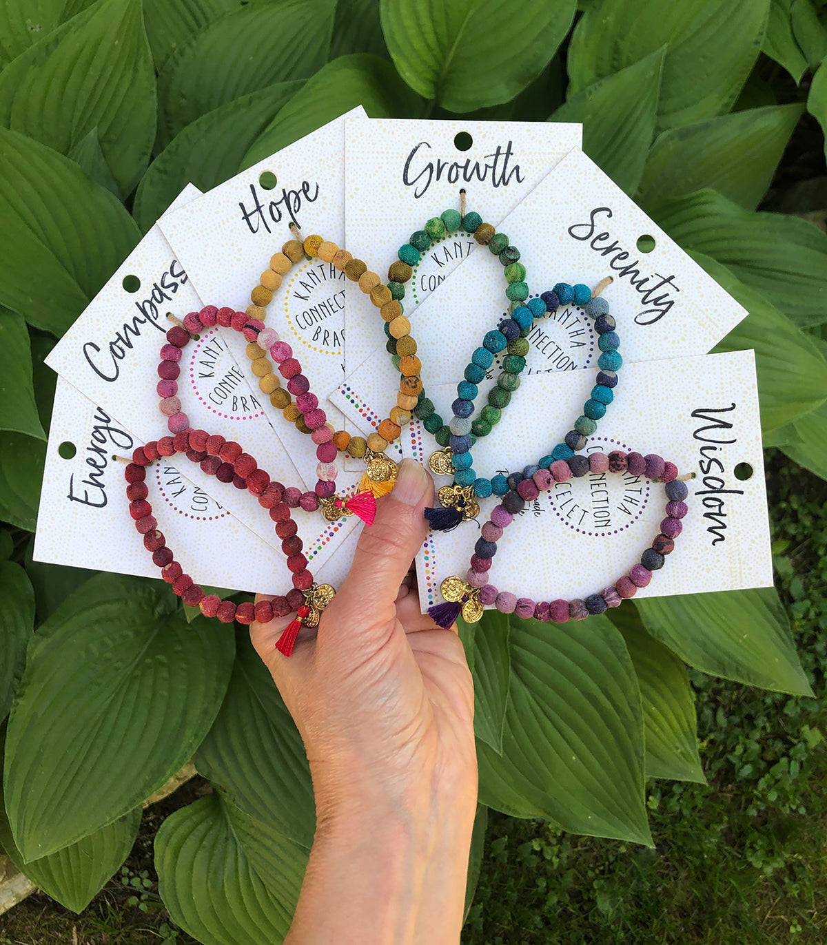 A hand holds out six carded bracelets, each a different color to create a rainbow.