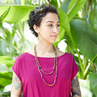 A woman in a pink shirt is adorned with a multicolored, beaded necklace.