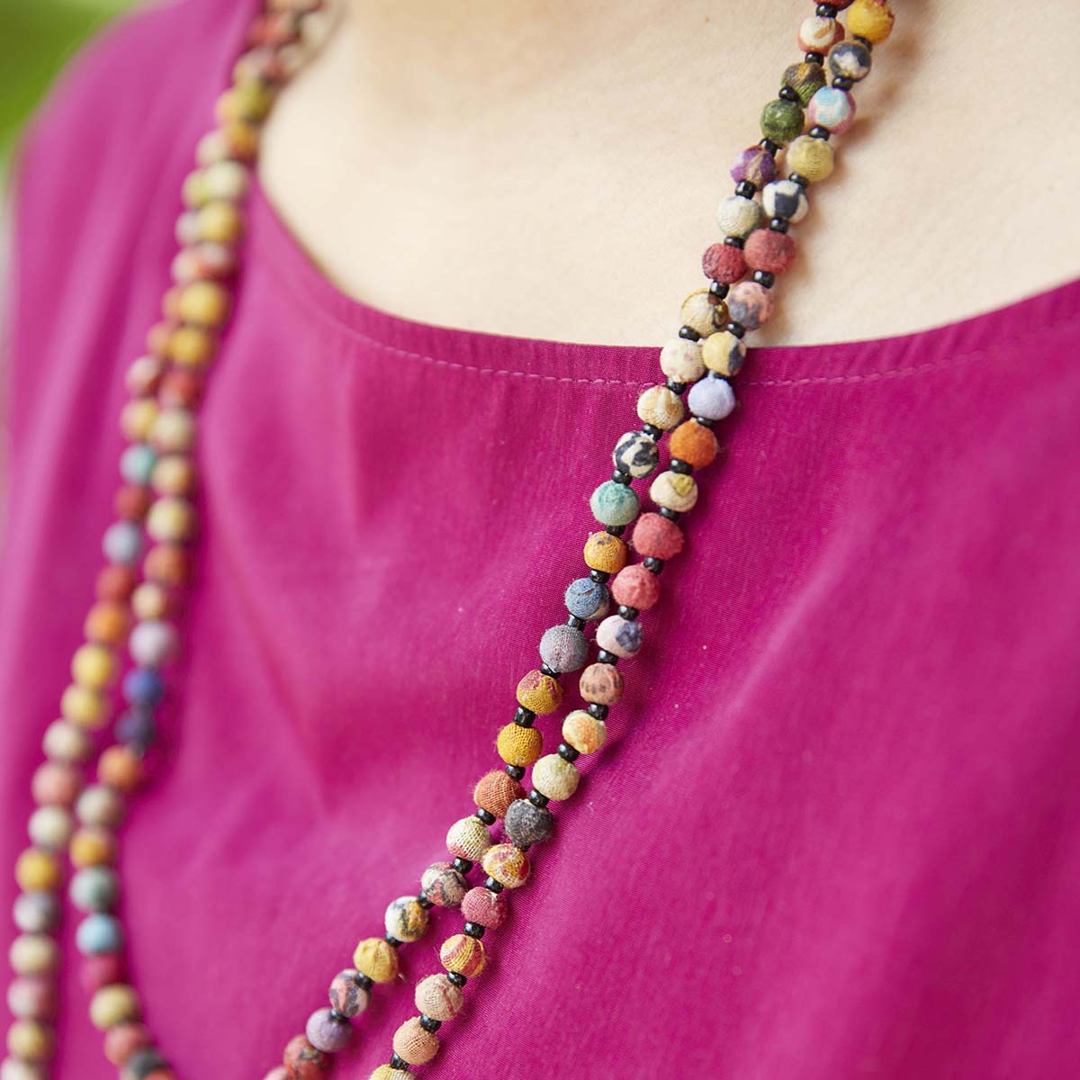 A close up of multicolor, beaded jewelry that alternates colorful fabric beads with small black seed beads.
