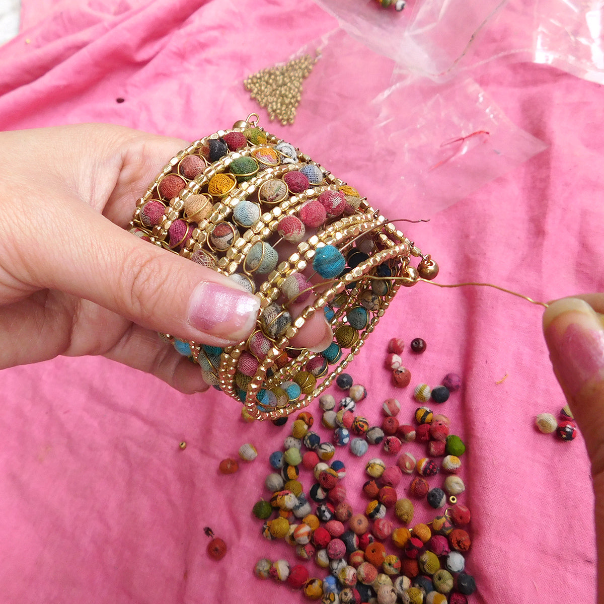 A close up of a woman's hands while she constructs a large beaded cuff bracelet.