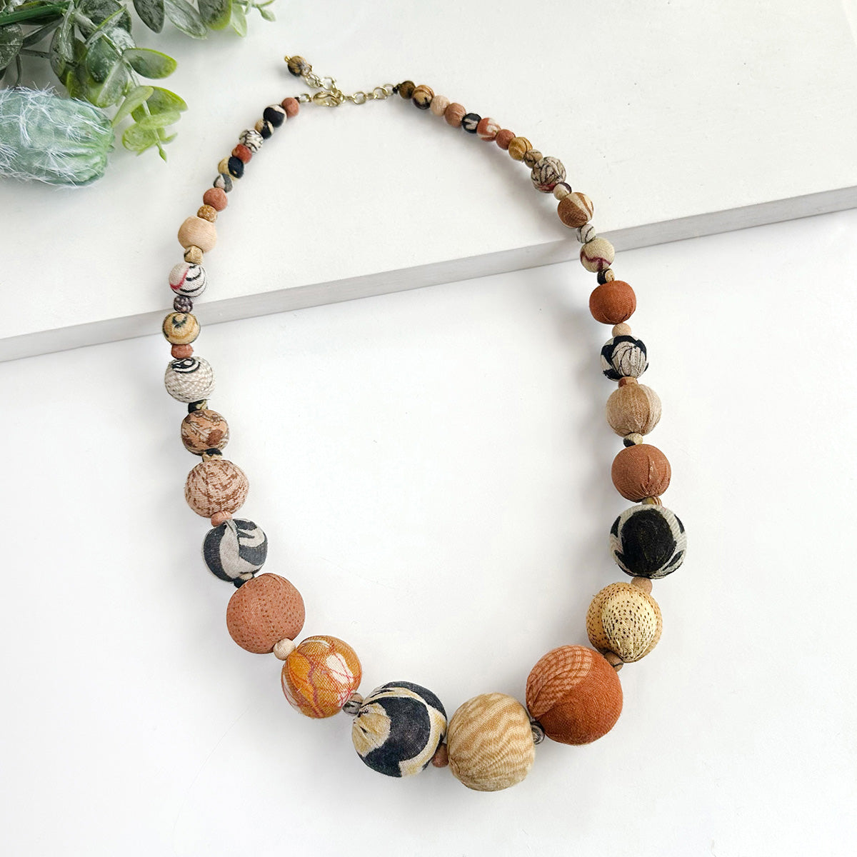 A beaded necklace of multi-toned brown & tan beads against a white background.