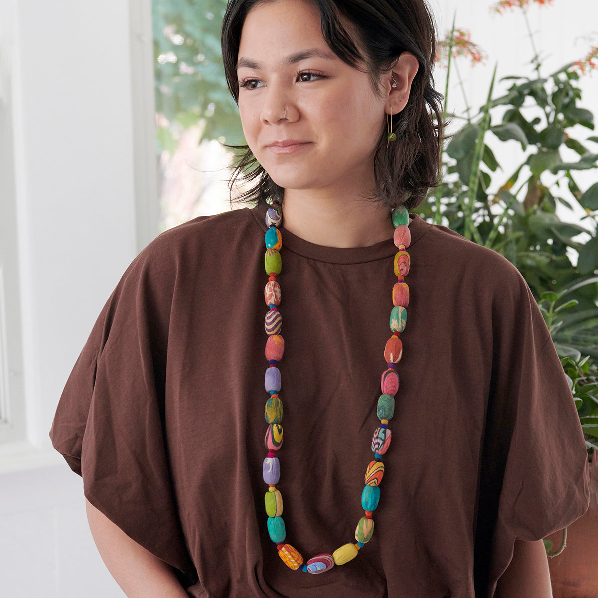 A young woman in a brown shirt and multicolored, beaded jewelry.