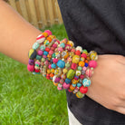 A close up of a woman's wrist and the twelve multicolor beaded bracelets she wears.