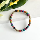 A multicolor beaded bracelet rests on a white background with a green and yellow flower in the top left corner.
