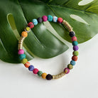 A multicolor beaded bracelet rests on a green leaf.