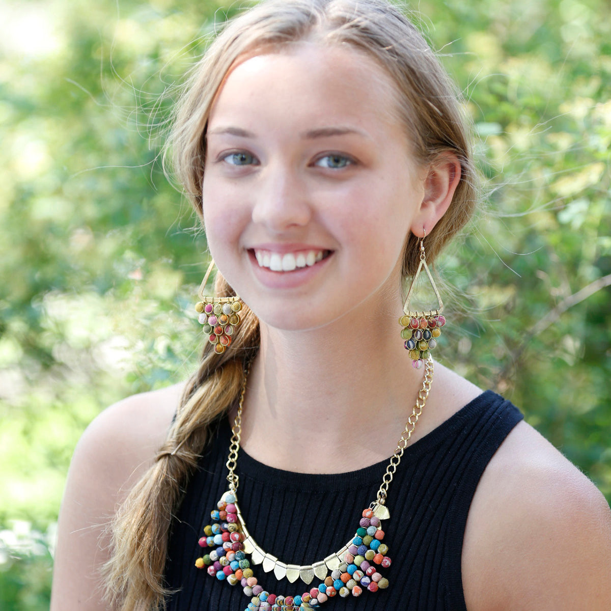 A woman in a black shirt and colorful, beaded jewelry smiles.
