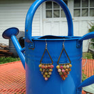 A pair of multicolored beaded earrings dangle from a bright blue watering can.