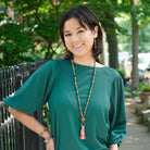 A woman in a teal shirt and multicolor, beaded jewelry smiles.