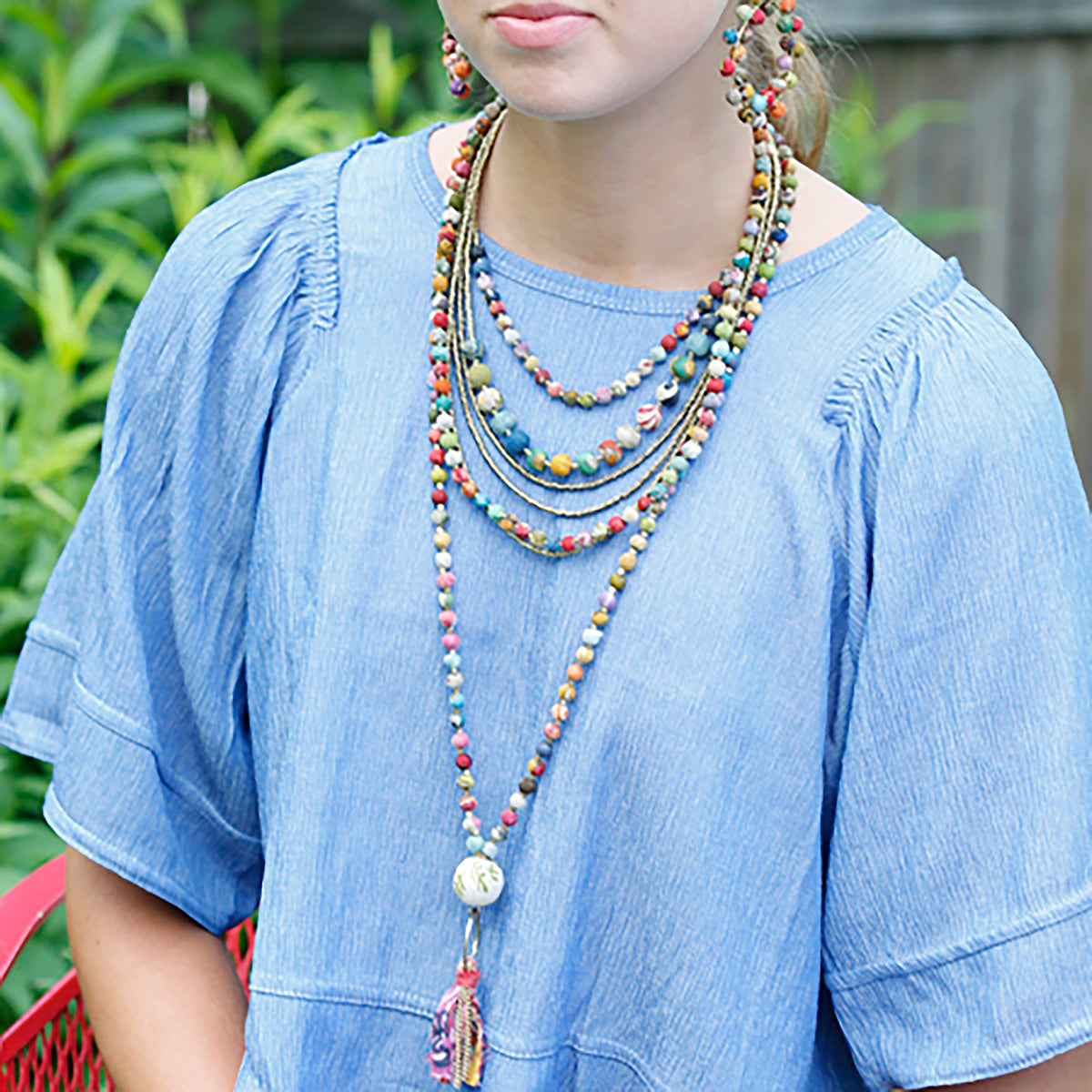 A close up of a woman in blue and her beaded, multicolor jewelry.