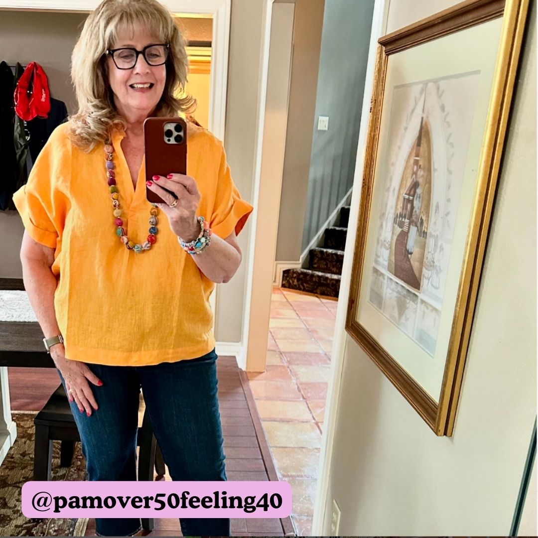 A woman in a yellow top takes a selfie in the mirror, showing off her beaded necklace.