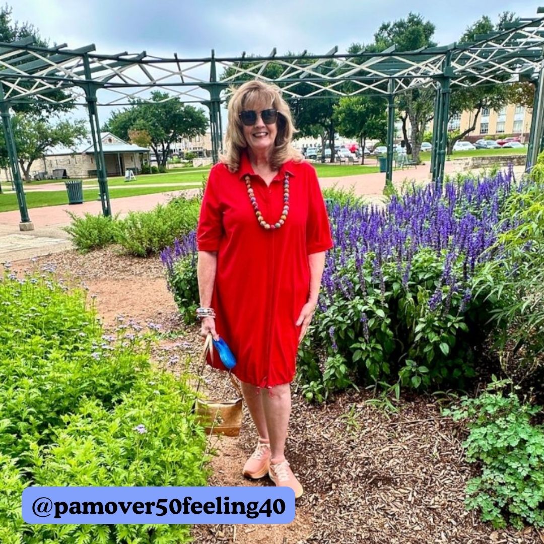 A woman in a red dress poses in a garden, showing off her beaded necklace.