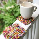 A white mug rests on a multicolored Sari Home Square Coaster