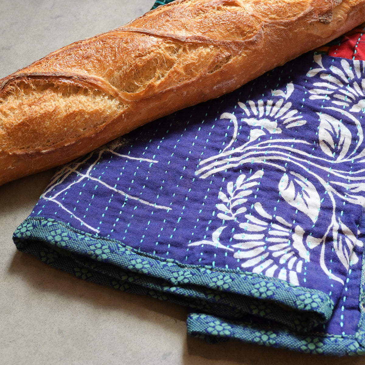 A baguette rests on a Sari Home Tea Towel.