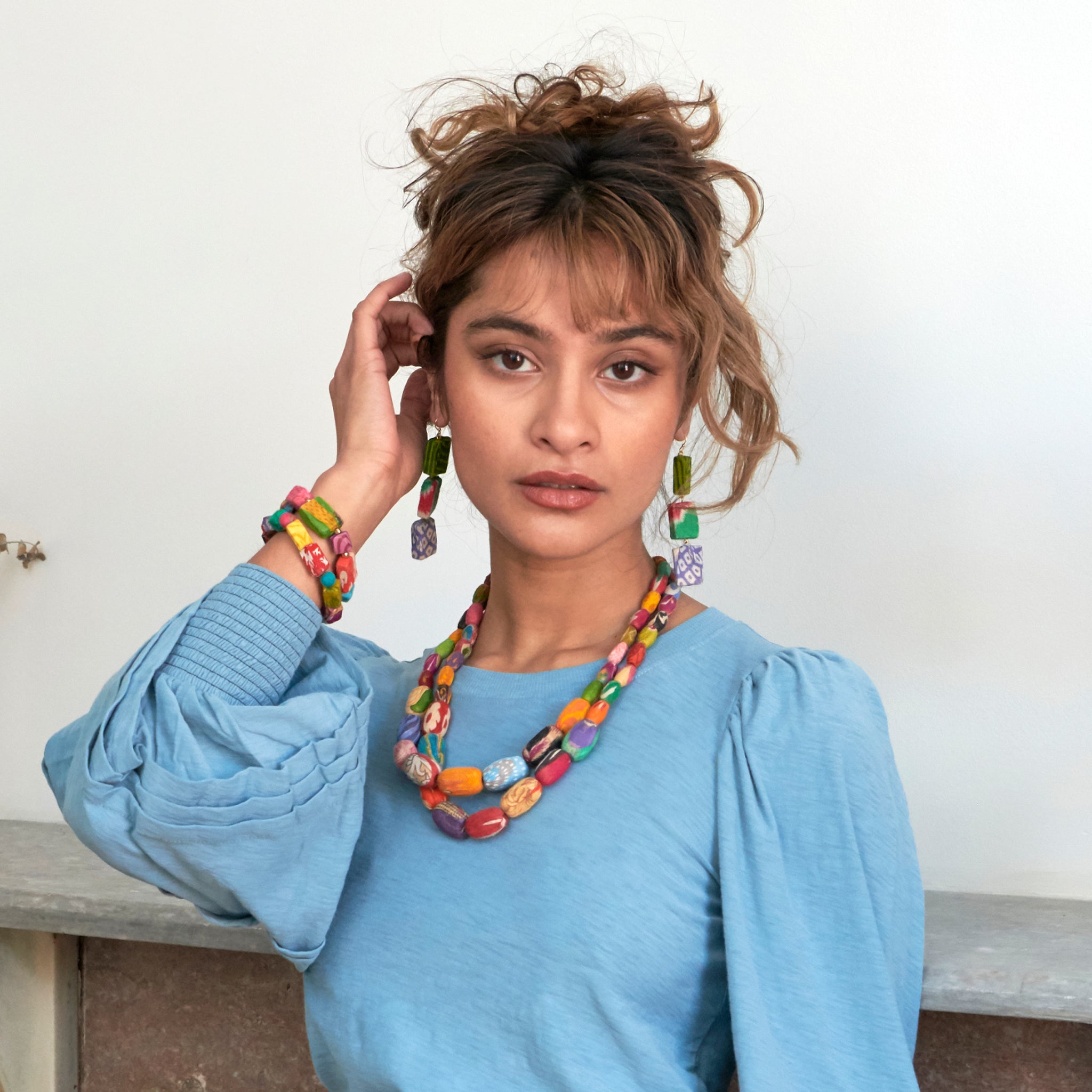 A woman looks at us while modeling colorful beaded jewelry.