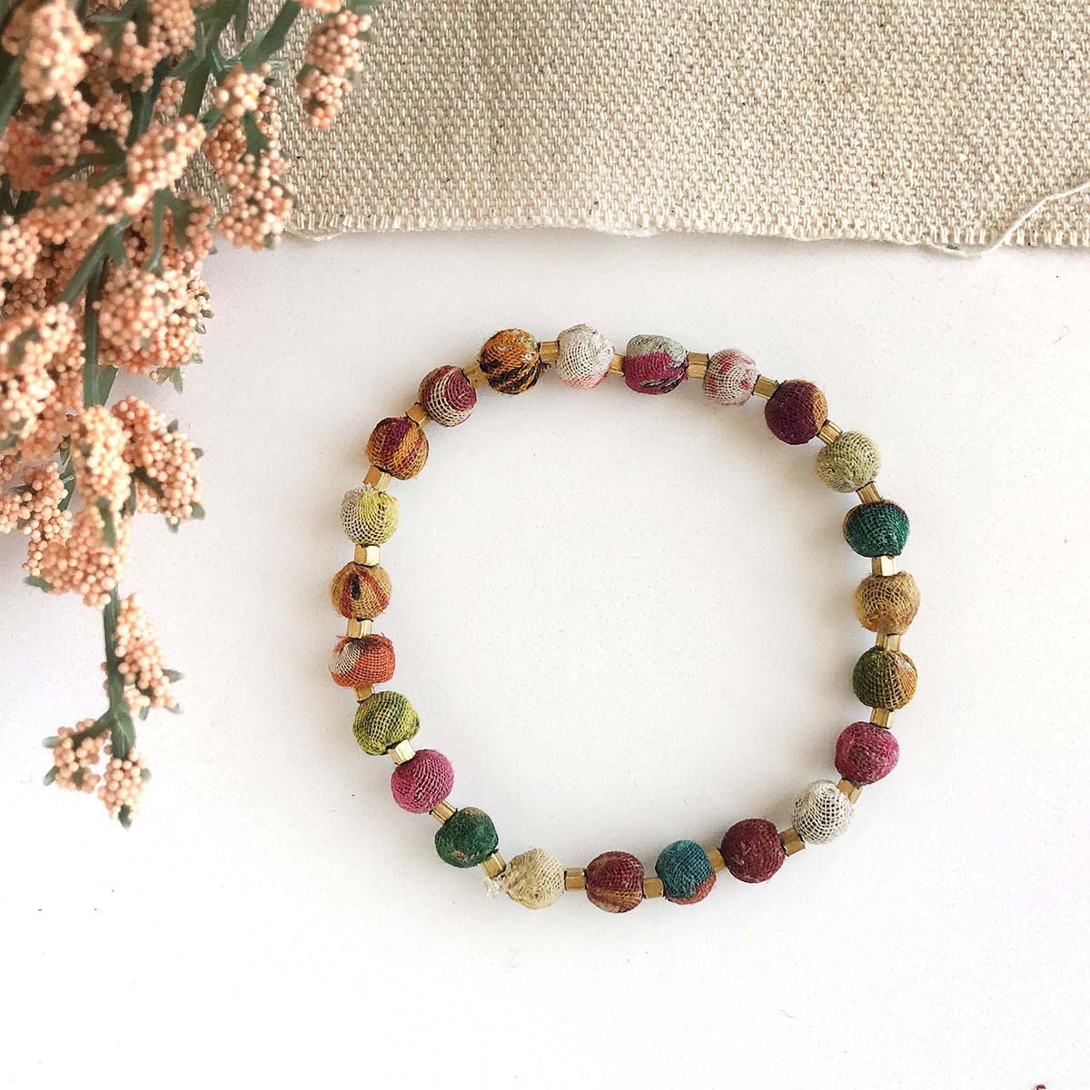 A multicolor, beaded bracelet against a white background with pink flowers in the top left.