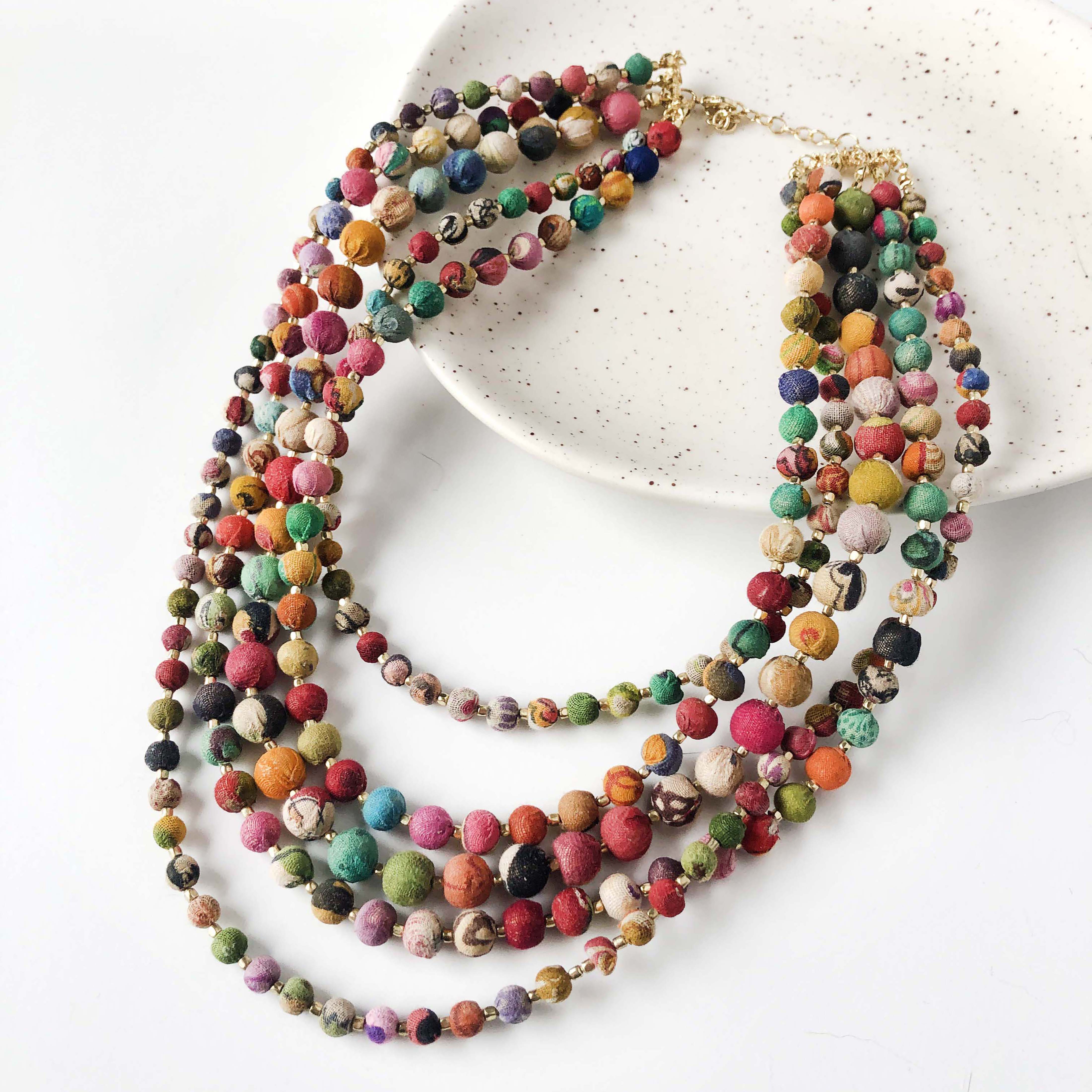 A five-strand multicolor necklace hangs off a white plate on a white surface.