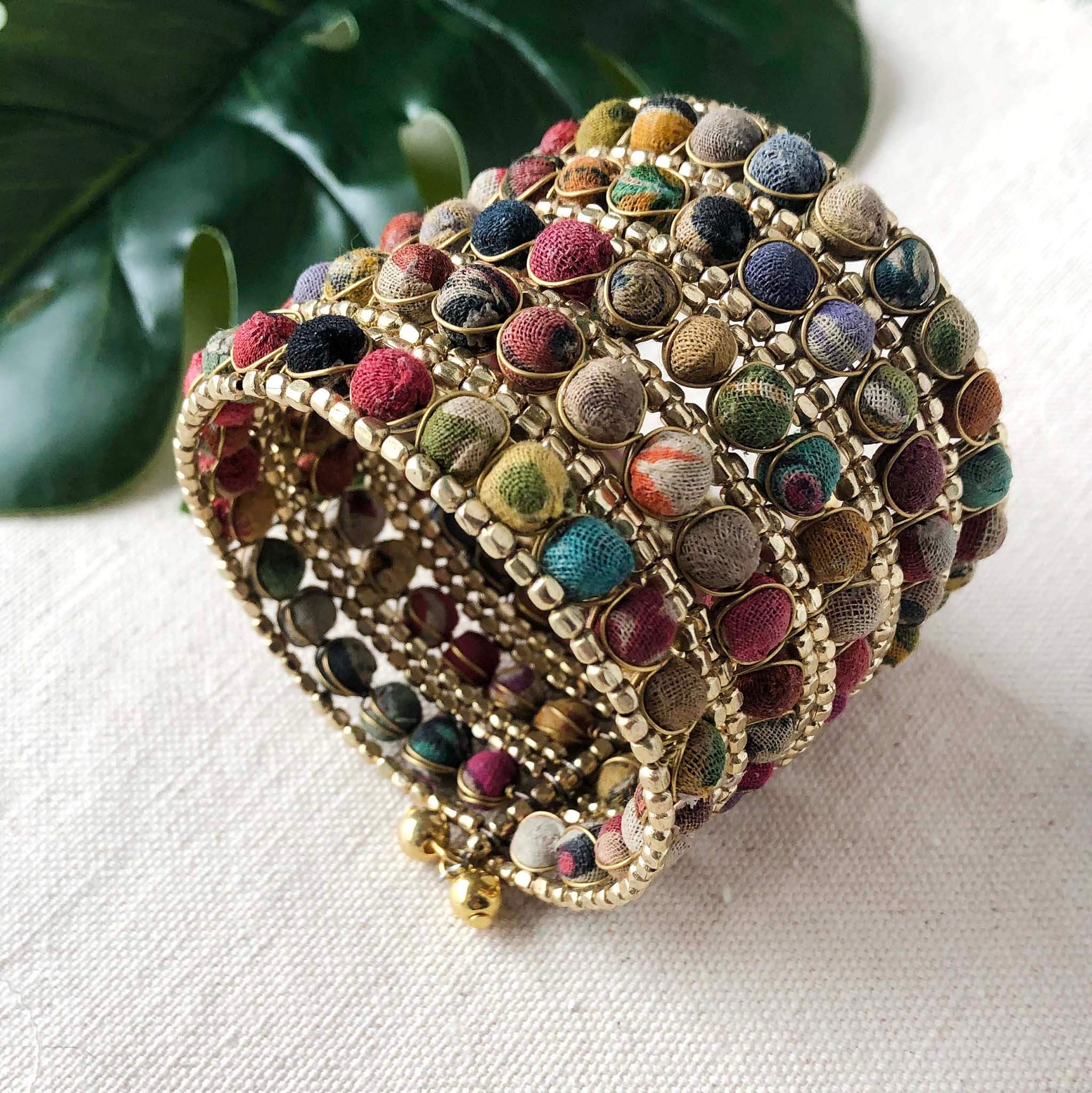 The top of a large cuff bracelet made from colorful textured fabric and gold beads.