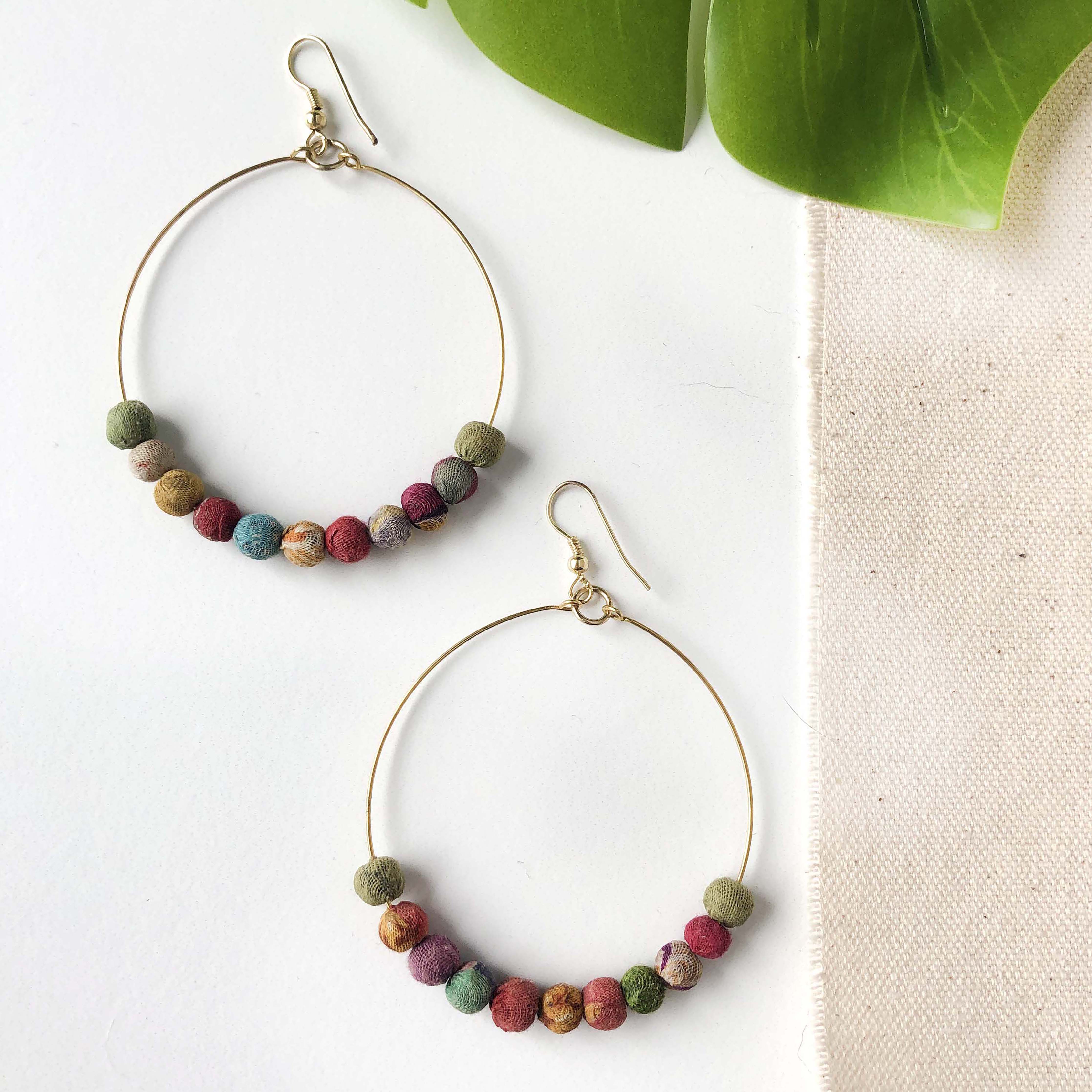A pair of hoop earrings with small multicolor beads against a white background with leaves.