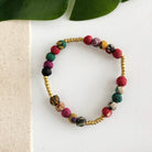 A multicolor and gold beaded bracelet against a white background with a green leaf in the top corner.