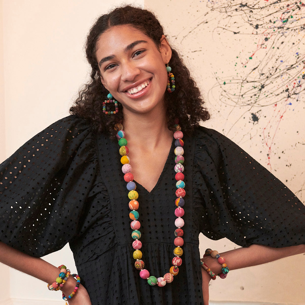 A woman in a black dress smiles while wearing a multicolor, beaded necklace and earrings.