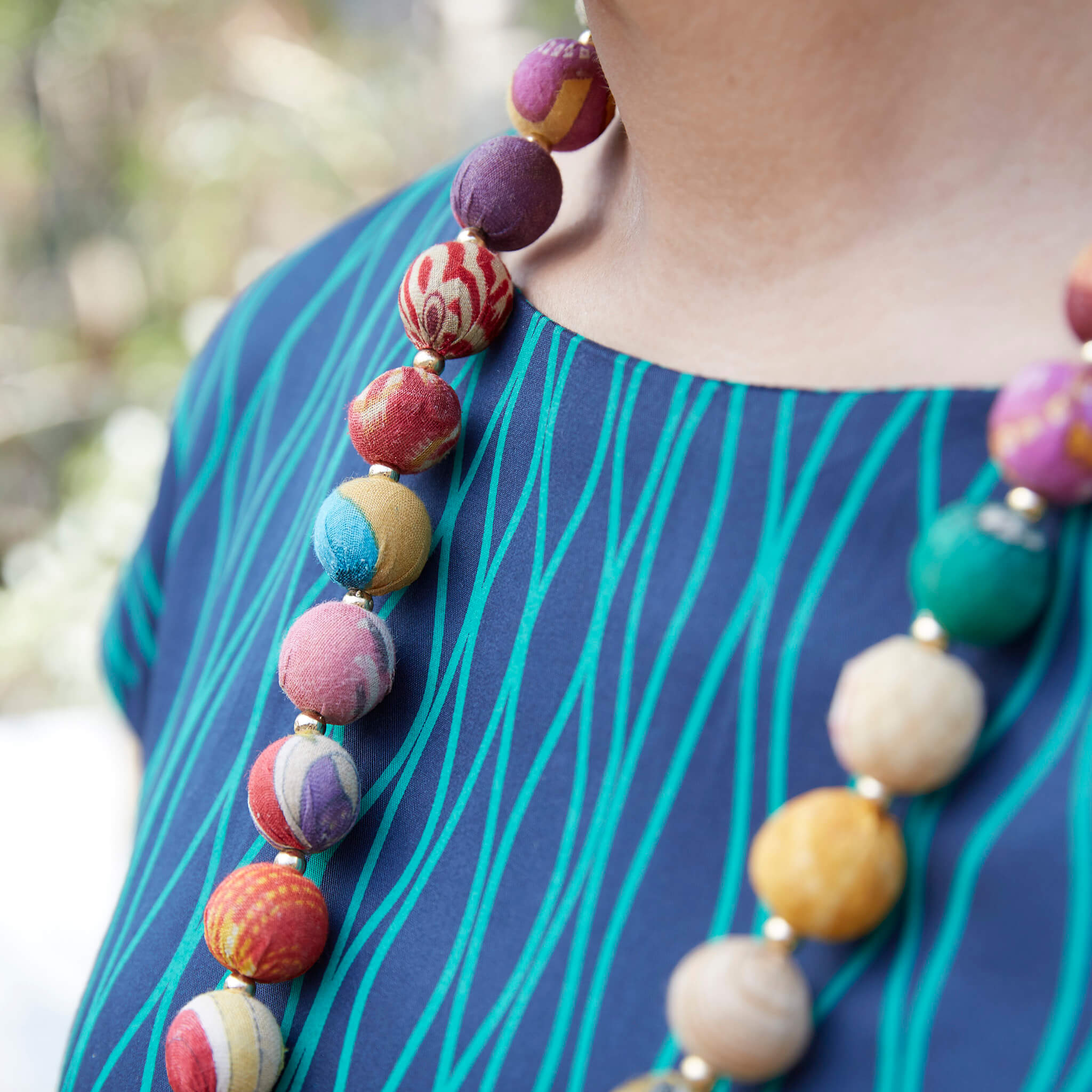A close up of a woman's shirt and her multicolor beaded necklace.