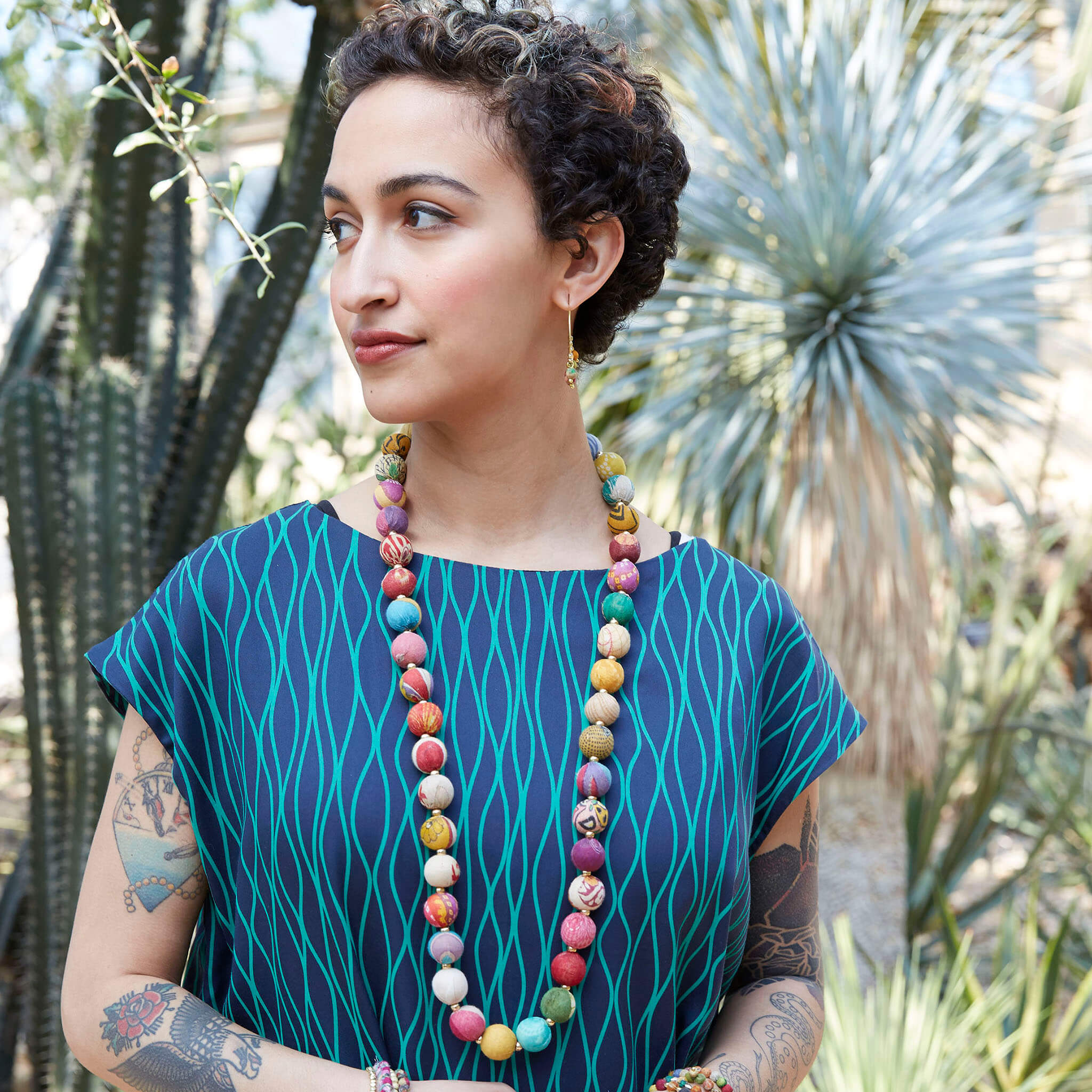 A woman with a patterned blue shirt and a multicolor beaded necklace.