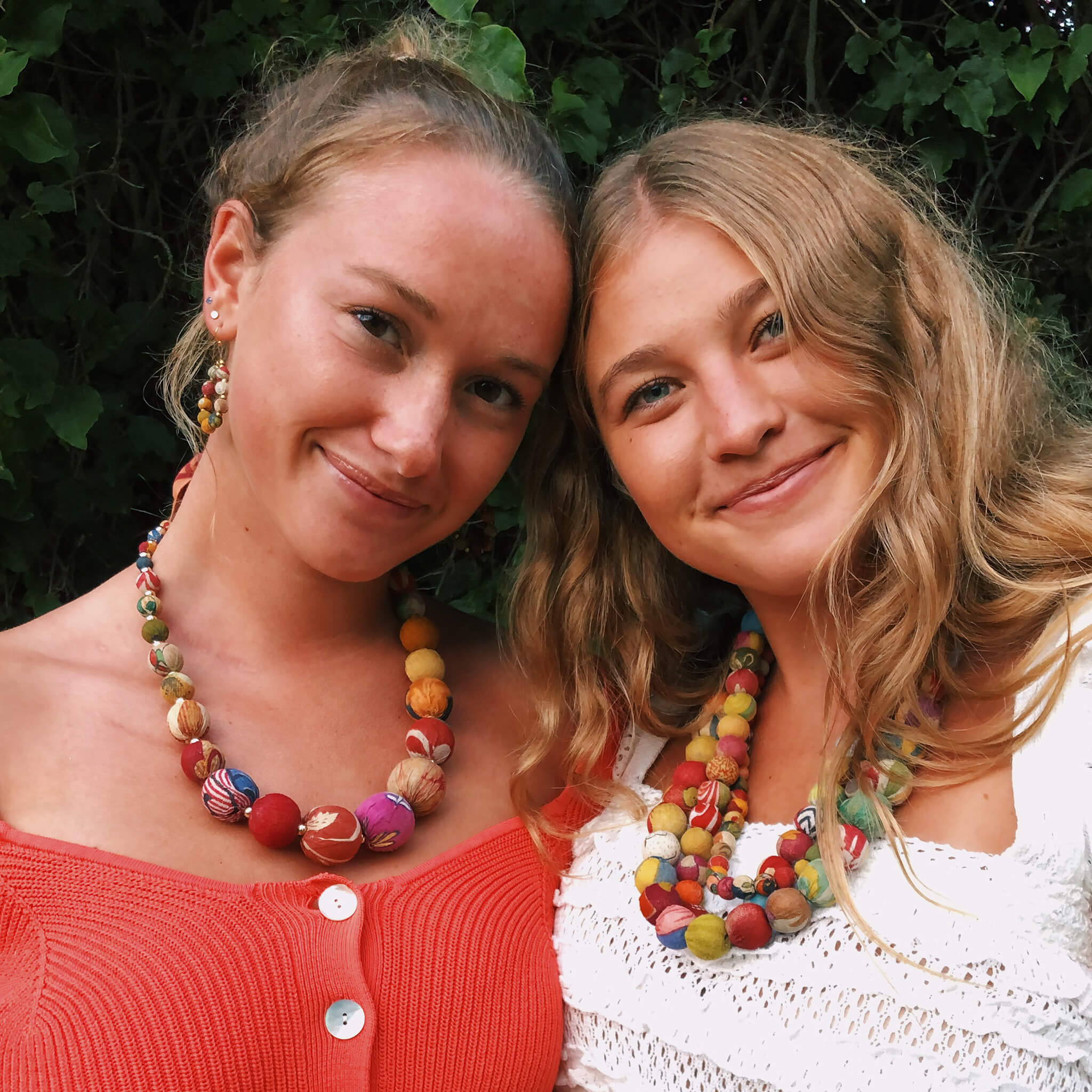 Two young women smile at while wearing colorful Kantha necklaces.