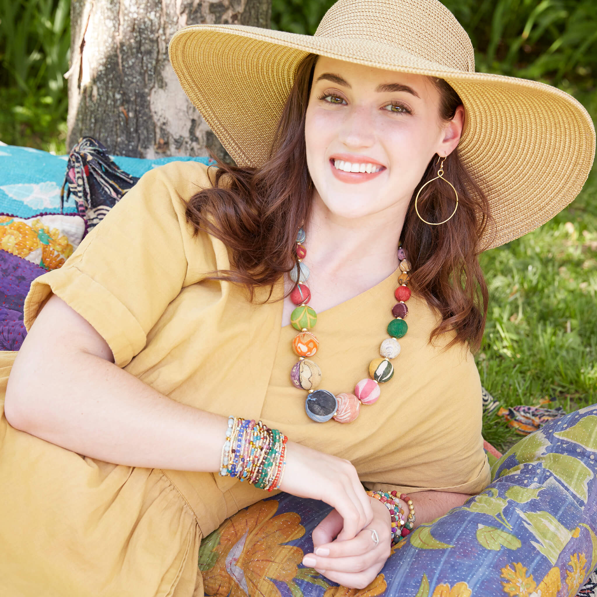 A woman in a yellow dress smiles and is adorned with multicolor, beaded jewelry.