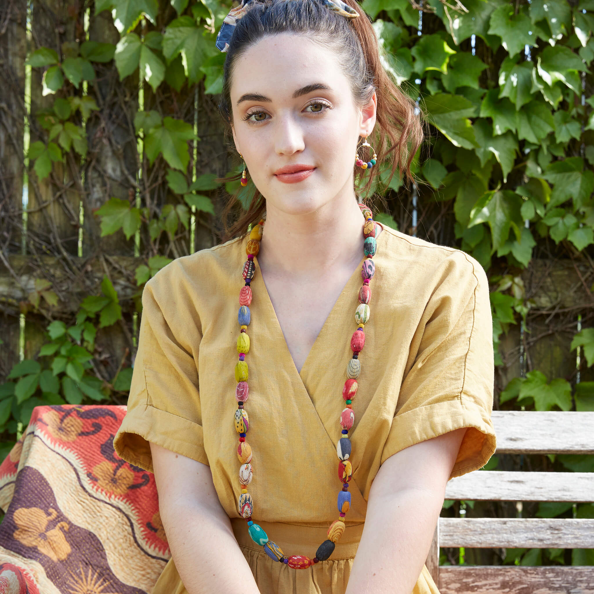 A woman in a yellow dress and multicolor beaded jewelry.