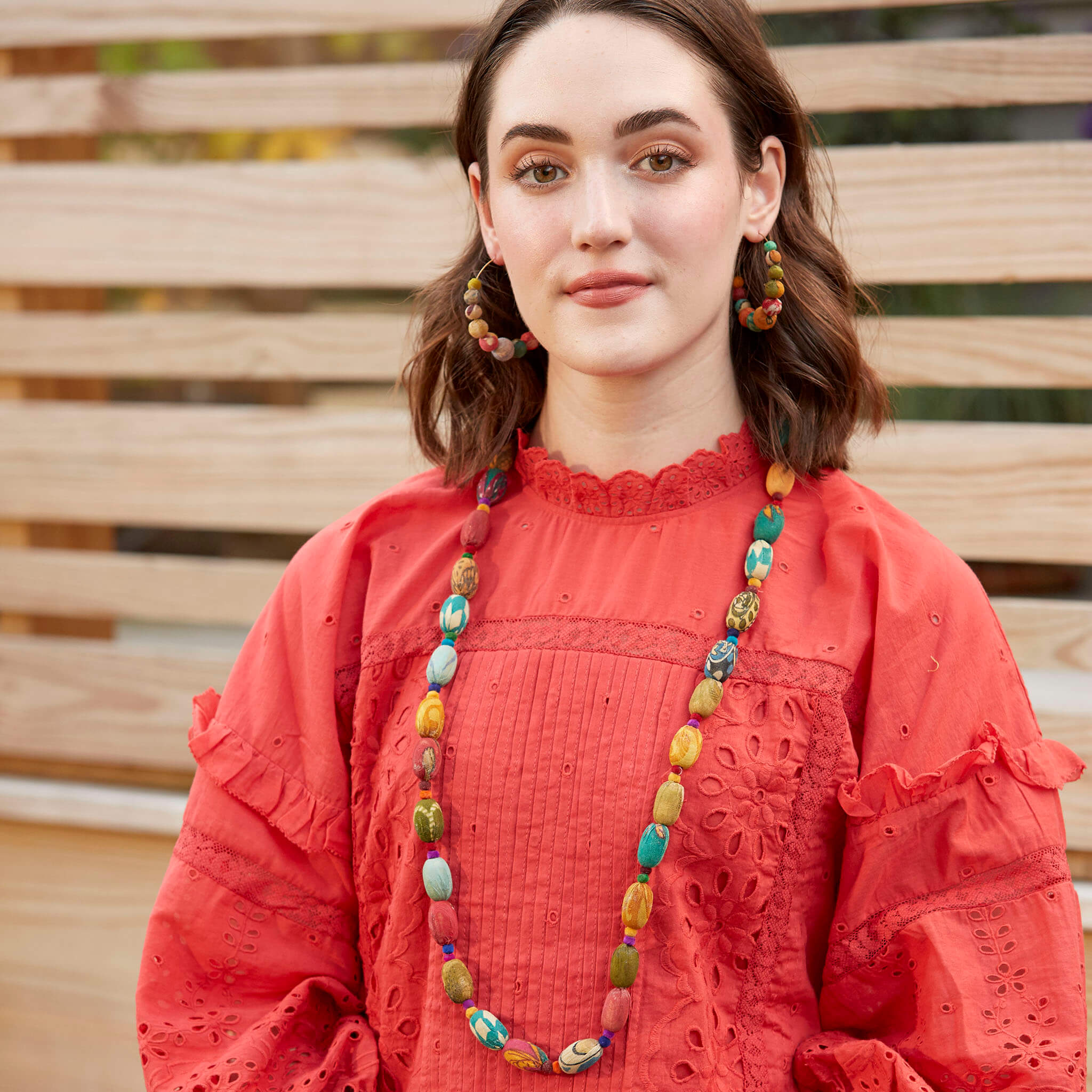 A woman in a red shirt and multicolor beaded jewelry.