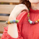 A woman in a red shirt holds her hand by her face, showing the large beaded bracelet on her wrist.