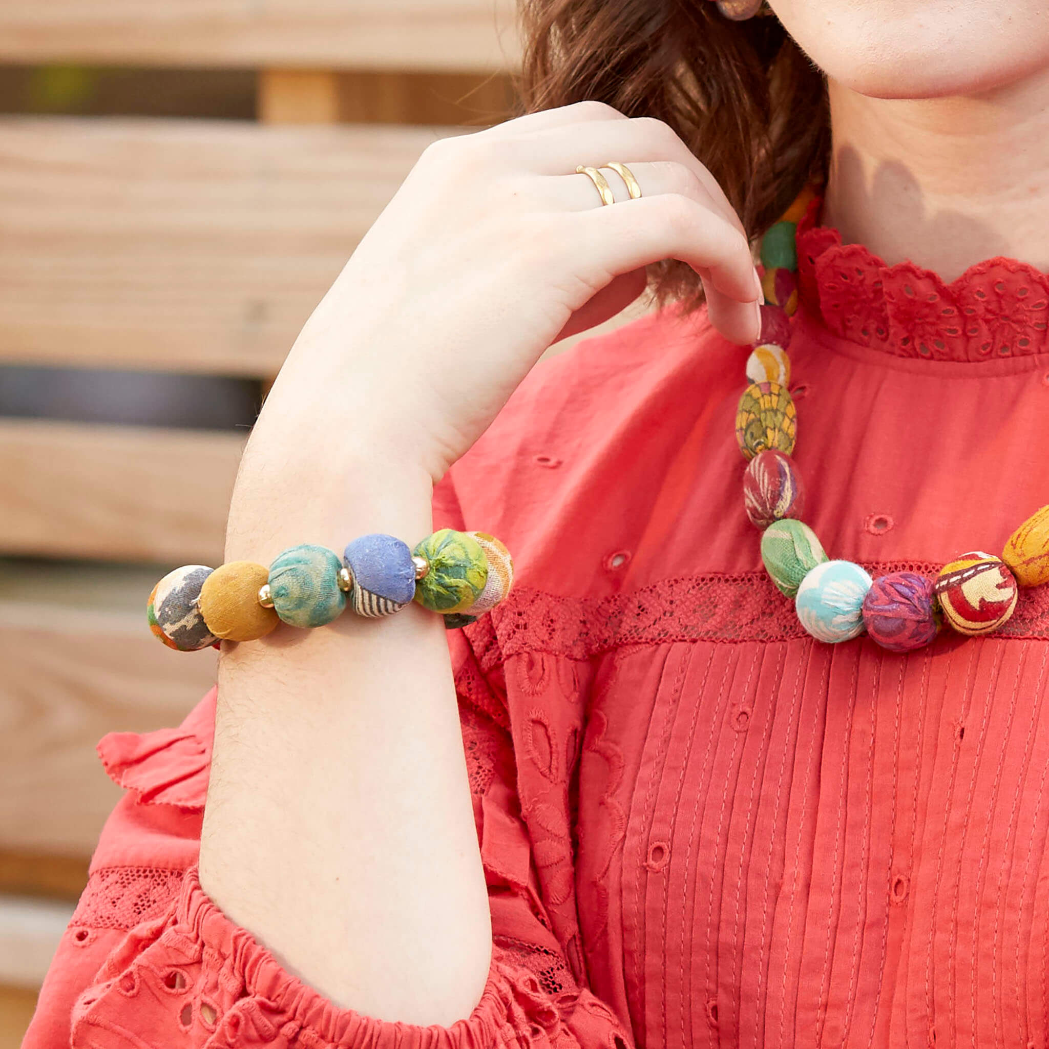 A woman in a red shirt holds her hand by her face, showing the large beaded bracelet on her wrist.