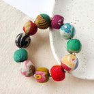 A large, multicolor beaded bracelet rests against a white plate and neutral background.