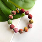 A multicolor beaded bracelet rests against a green leaf.